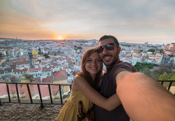 handsome tourists take selfie photo with view on Lisbon,Portugal from miradouro on sunny clear day holding portugal flag.Honeymoon loving romantic couple traveling to european city for holiday