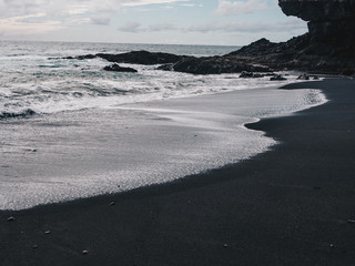 Stormy ocean waves with white foam hitting black sand beach of Ajuy in Fuerteventura, Canary Islands, Spain. Dark clouds