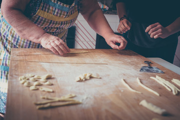 Process of production of pasta. woman hands make fresh pasta on wood board kitchen table