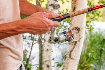 Naklejka premium Fisherman hands with fishing rods is fishing against background of beautiful nature and lake or river. Camping tourism relax trip active lifestyle adventure concept