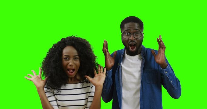 Portrait shot of the young African American young couple looking at each other and then screaming with scared faces to the camera on the green screen. Chroma key.