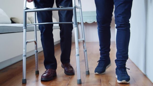 Male nurse helping senior man use walking frame, low section