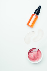 top view of cosmetic bottle with pipe, eye patches, spoon and pink mask in container isolated on white