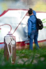 A few used paint cans against the background of the space with the wall on which the young guy draws a large graffiti drawing. Modern art of drawing walls in graffiti
