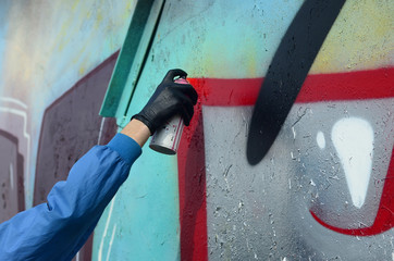 A hand with a spray can that draws a new graffiti on the wall. Photo of the process of drawing a graffiti on a metal wall. The concept of street art and illegal vandalism