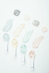 flat lay with spoons, different clay powder and colorful clay mask smudges placed in row on white surface
