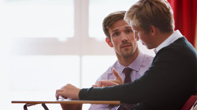 Male College Student Sitting Examination Talking With Teacher