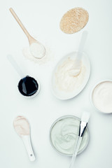 flat lay with sponge, various clay masks in containers, plate, clay powder, spoons and brush isolated on white surface