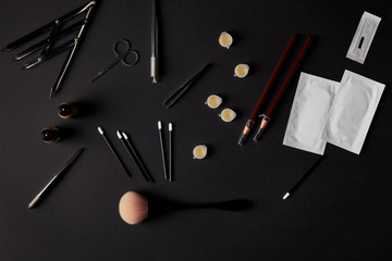 top view of brushes, pencils, cosmetics and tools for permanent makeup on black