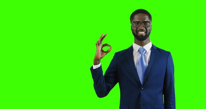 Close up of the handsome young African American businessman standing on the chroma key background with serious face, doing ok gesture with fingers and smiling. Green screen.