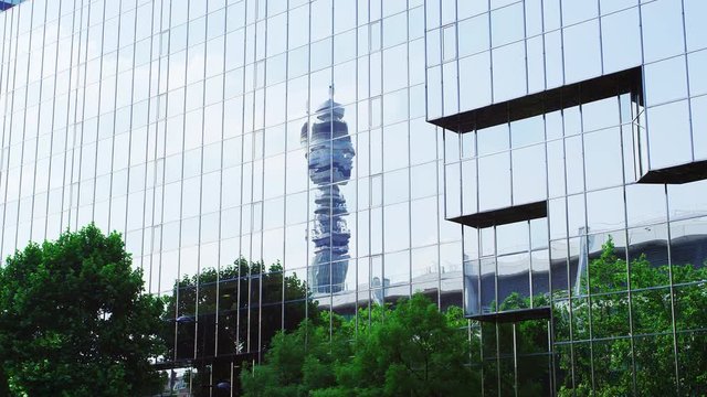 LONDON - MAY, 2017: BT Tower and treetops reflected in modern glass fronted buildings against blue sky, London, W1