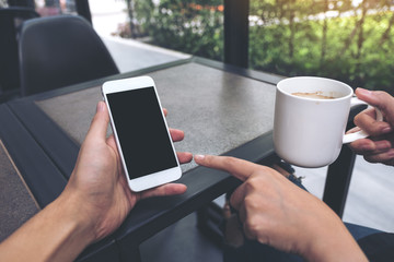 Mockup image of two people looking and pointing at a white mobile phone with blank black desktop screen in cafe