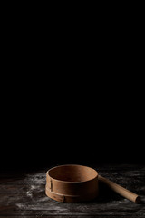 closeup shot of sieve and rolling pin on wooden table covering by flour isolated on black background