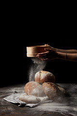 cropped shot of female baker sieving flour over various types of bread on sackcloth isolated on...