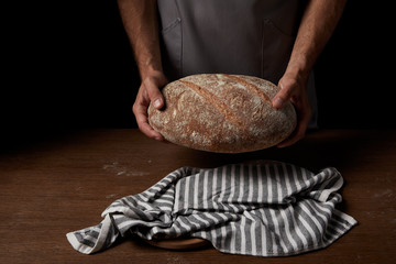 partial view of male baker in apron holding bread over wooden table