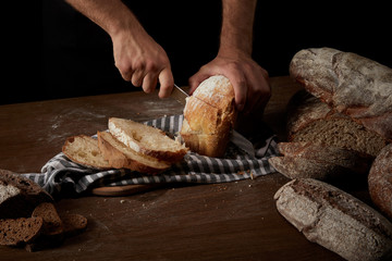 cropped shot of male baker cutting bread by knife on sackcloth on wooden table