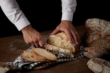 partial view of male baker cutting bread by knife on sackcloth on wooden table