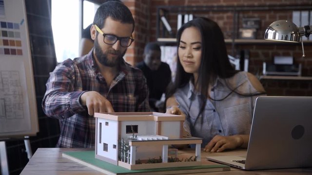 Charming Asian girl and man coworking on hi-tech house miniature creating modern and developed accommodation