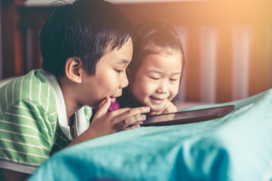 Asian children watching video and playing game on digital tablet.