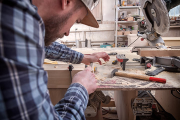 Close-up of craftsman hands in gloves measuring wooden plank with ruler and pencil on workbench. Concept of woodwork and handcraft.