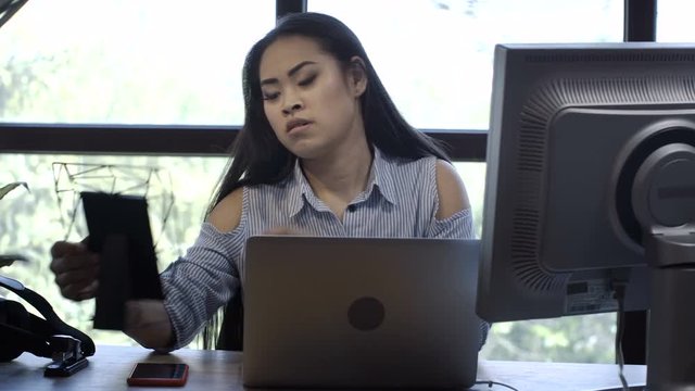 Young beautiful Korean woman working at table with computers looking sad and missing family while looking at photo in frame