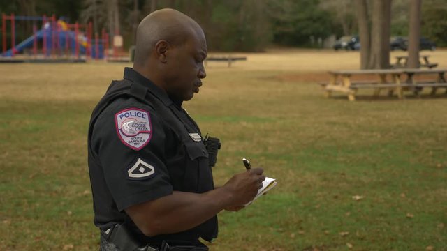 An African American police officer takes a notebook out of his uniform pocket to write a note.