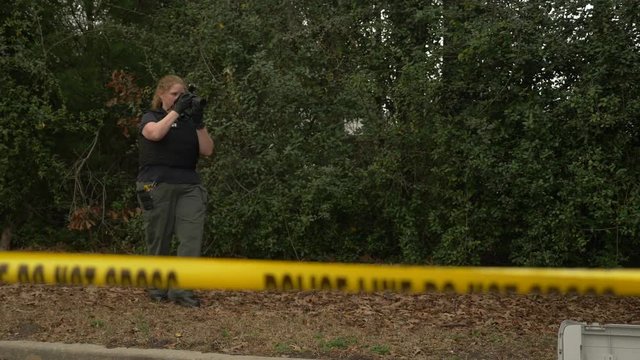 A crime scene investigator walks around and takes pictures of a crime scene with a camera.
