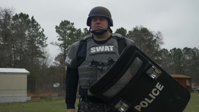 A SWAT team police officer holds a riot shield ready for tactical action.