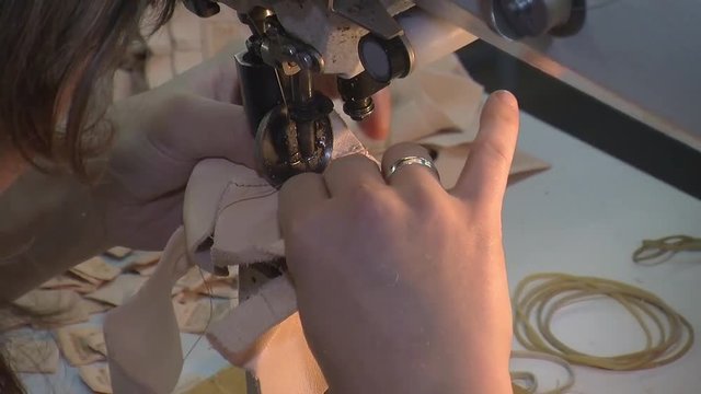 Worker sews leather for shoe production with sewing machine