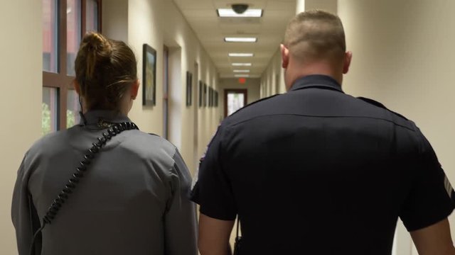 Two police officers walk down the hallway of a police department building.