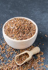 A wooden bowl and scoop with linseed on a granite stone background with copy space for your text.