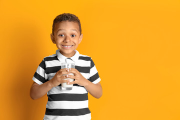 Adorable African-American boy with glass of milk on color background