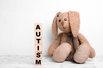 Toy bunny and wooden cubes with word AUTISM on table against light background