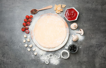 Dough and ingredients for pizza on gray background, top view