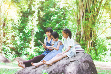 Three asian student girls sitting on the stone reading a book in garden at summertime