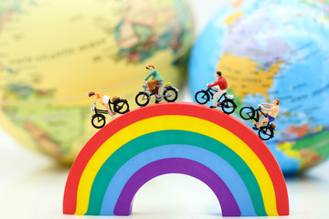 Miniature people : Travelers riding bicycle on rainbow with world map,travel concept.