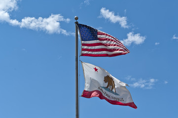 An American flag and a California Republic flag weaving on a blue sky background. Concept for freedom, patriotism and independence