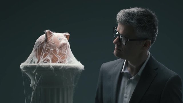 Businessman and dusty piggy bank with cobwebs