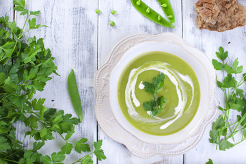 Cream soup of green peas and Parsley. Healthy lunch in a white plate on a white wooden background, Copy space.