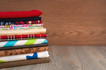 A stack of multi-colored fabric for sewing. Many different fabrics are stacked on a table. Fabric for sewing clothes and bed linen.