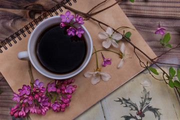Obraz na płótnie Canvas Beautiful violet lilac flowers with white cup with coffee or tea, on a wooden background