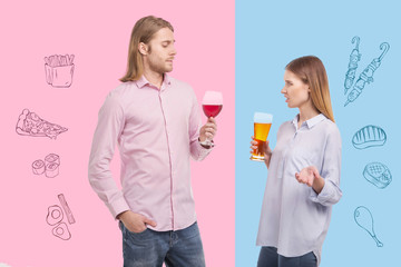 Disgusting drink. Expressive young woman holding a glass of beer and frowning while her calm husband feeling satisfied with his tasty wine