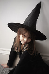Girl in black witch costume sitting near wall