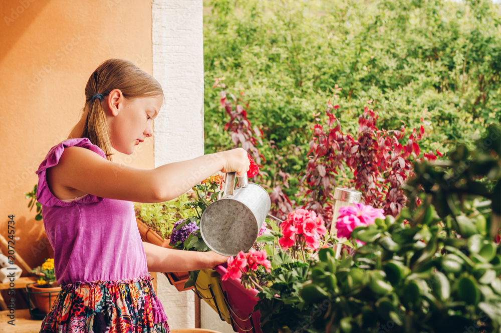 Wall mural Adorable little girl watering plants on the balcony on a nice sunny day