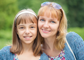 Happy family outdoors in summer day. Mother Day. Portrait of mother and daughter smiling into the camera lens. Woman with child having fun together during walk in the park.