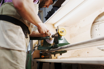 .Unrecognizable man's hands hold chisel near lathe, joiner working at small wood carpenter. An artisan carves a piece of wood using a manual lathe