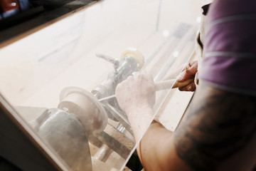 Unrecognizable man's hands hold chisel near lathe, joiner working at small wood carpenter. An artisan carves a piece of wood using a manual lathe