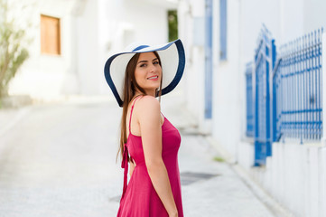Travel Europe for summer holiday. Portrait of beautiful woman visitting old villages in Greecem with sun hat and summer dress.