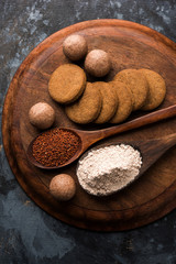 Nachni / Ragi laddu and biscuits or cookies made using  finger millet, sugar and ghee. It's a healthy food from India. Served in a bowl or plate with raw whole and powder. Selective focus