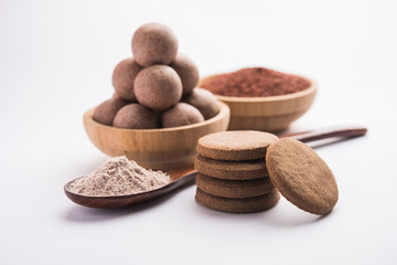 Nachni / Ragi laddu and biscuits or cookies made using  finger millet, sugar and ghee. It's a healthy food from India. Served in a bowl or plate with raw whole and powder. Selective focus